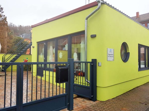 Grün-gelb gestrichenes Gebäude am Standort Annweiler mit einem Metallzaun und Eingangstor