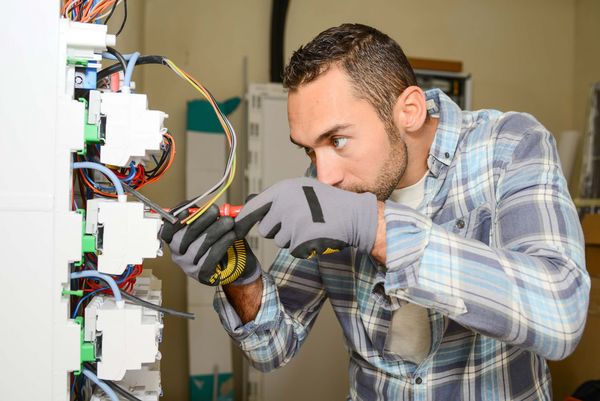 Ein Techniker mit Werkzeug und Handschuhen arbeitet konzentriert an Kabelverbindungen