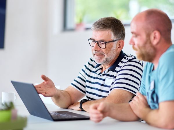 Zwei Männer sitzen am Computer und besprechen, was sie dort sehen (nicht sichtbar)